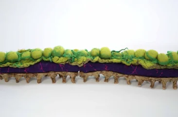 Textiel als taal. Een langwerpig viltkunstwerk met groene bollen en paarse ondergrond.